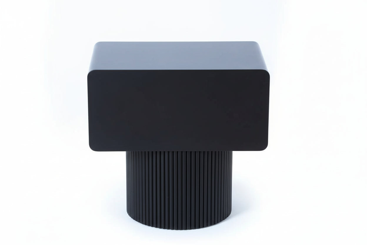 Black cube-shaped stool with ribbed cylindrical base on a light wooden floor.