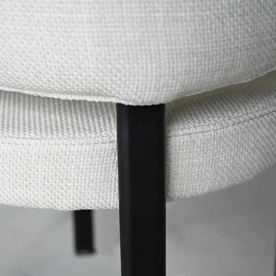 Close-up of a chair with white cushioned seat and black metal legs on a neutral background