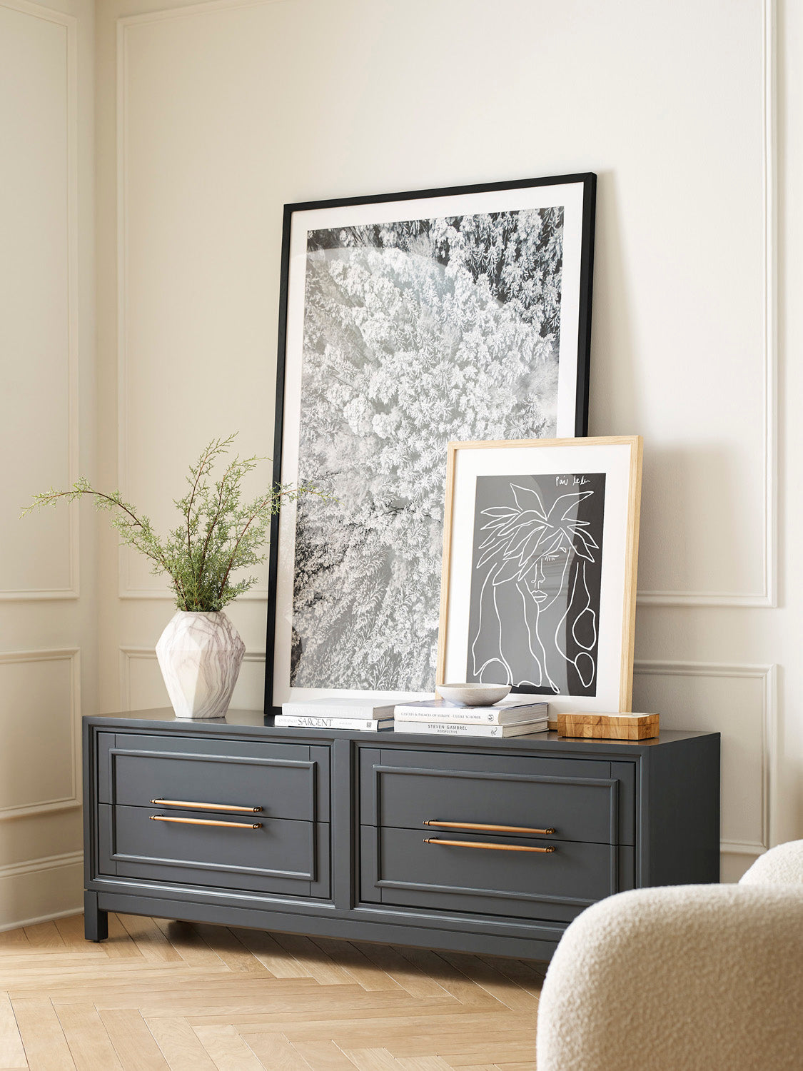 Gray dresser with gold handles in a room with framed artwork and decor.