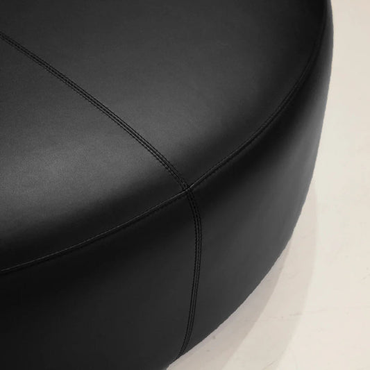 Close-up of a black leather seat with visible stitching on a beige background