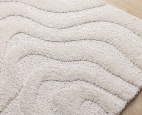 Close-up of a textured beige rug with wavy pattern on a wooden floor.