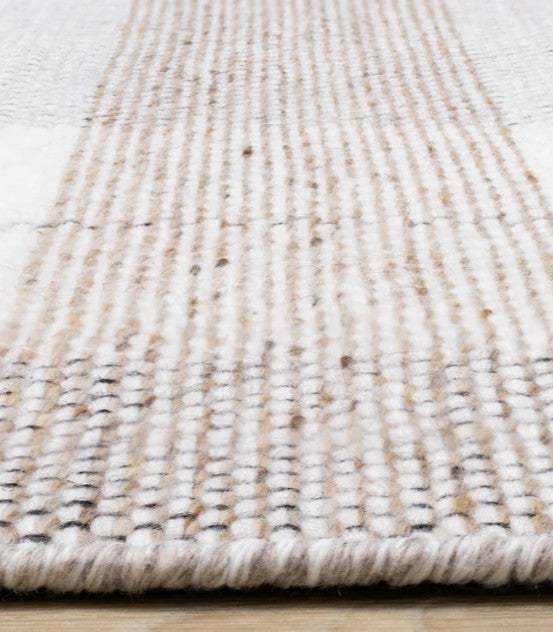 Close-up of a textured beige and white rug on a light wooden floor.