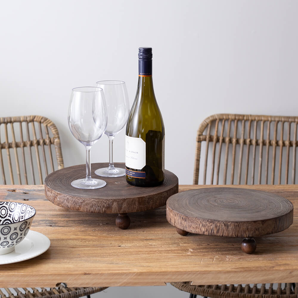 Wine bottle with two glasses on a wooden tray on a table with wicker chairs.