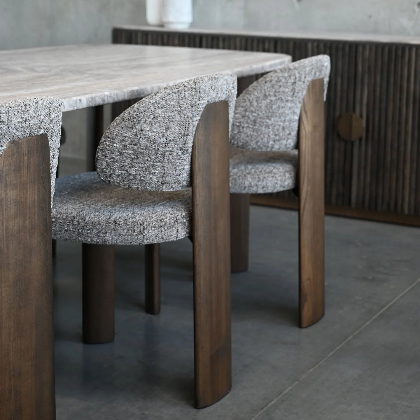 Dining table with wooden legs and chairs in a room with concrete walls and floor.