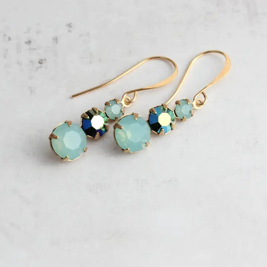Gold earrings with green gemstones on a light gray background