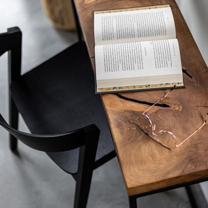 Open book on a wooden table with glasses next to it, black chair in the foreground