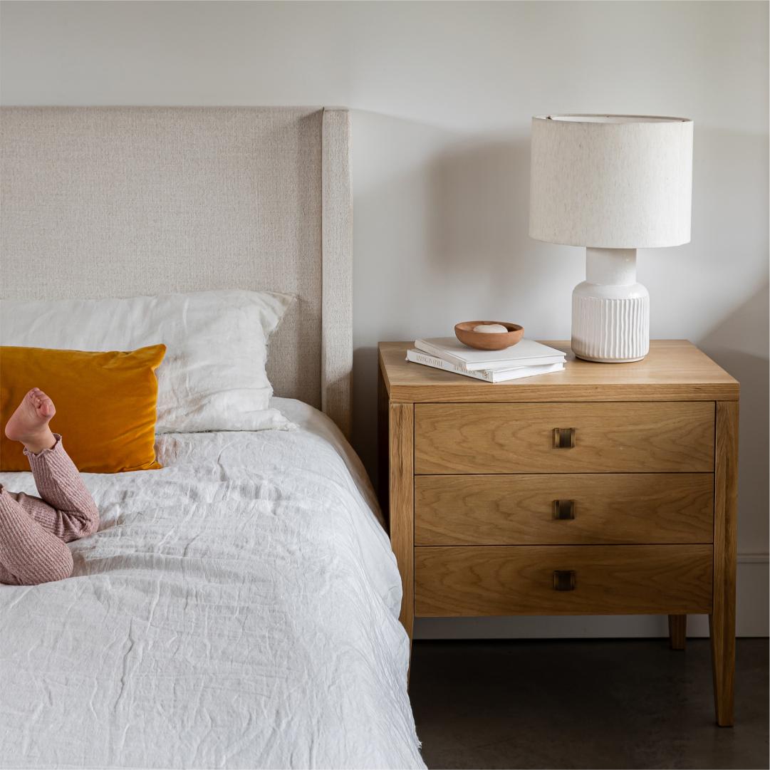 Bedroom with a bed and wooden nightstand featuring a lamp and books.