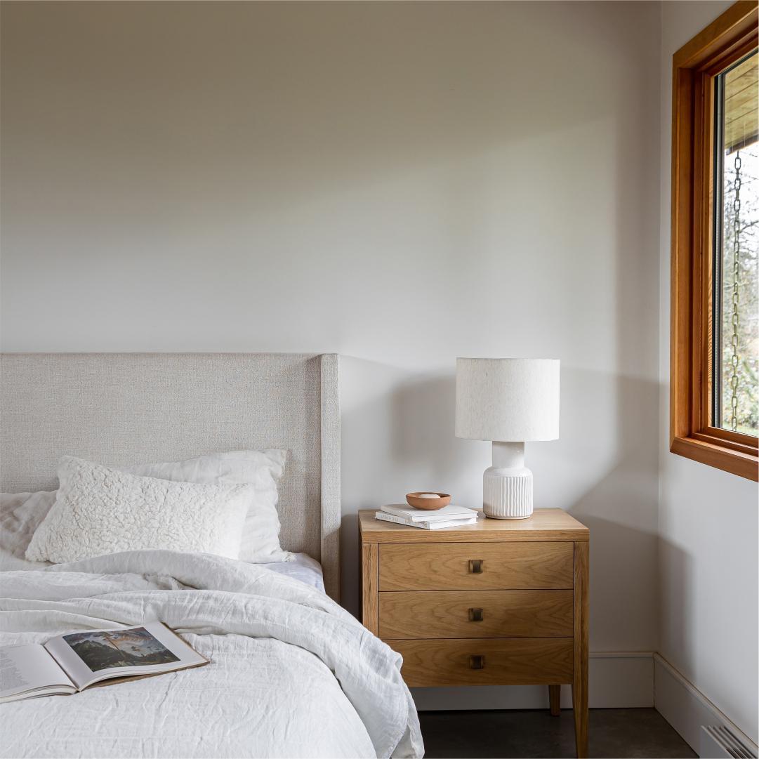 Bedroom with wooden nightstand, lamp, and open book near bed.
