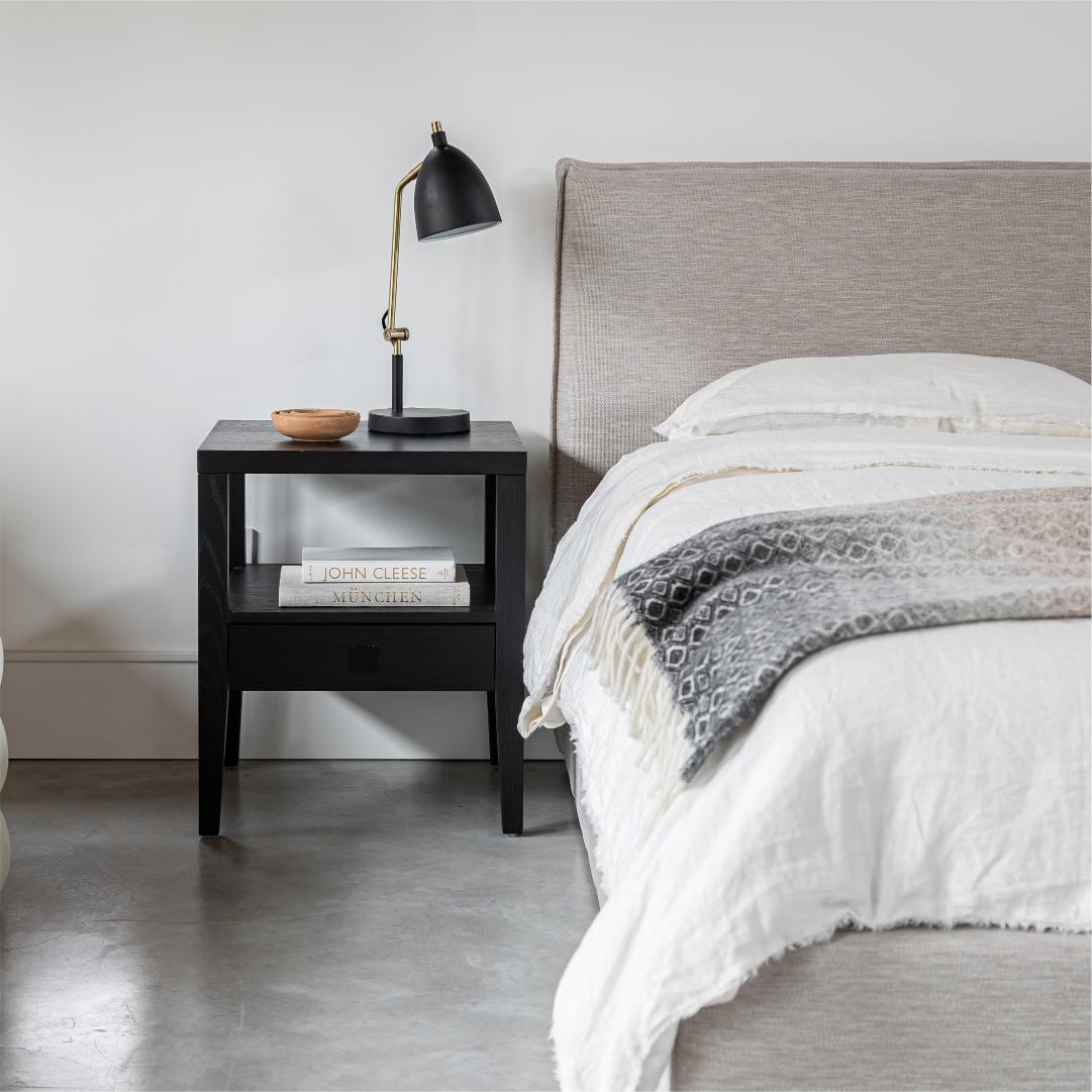 Bedroom with a bed and nightstand featuring a lamp and books.