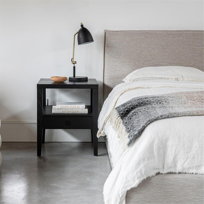 Bedroom with a bed and nightstand featuring a lamp and books.