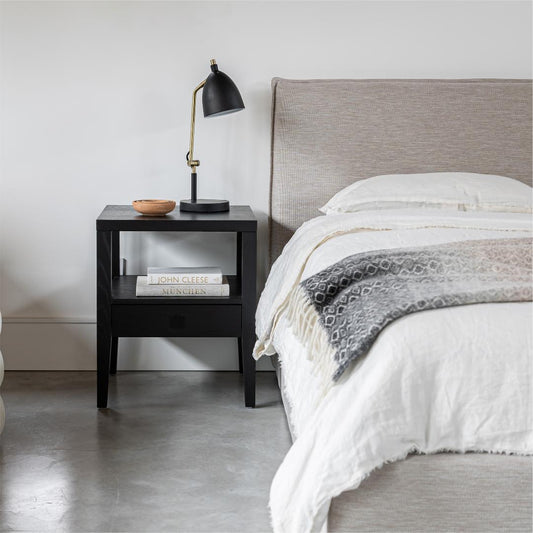 Bedroom with a bed and nightstand featuring a lamp and books.