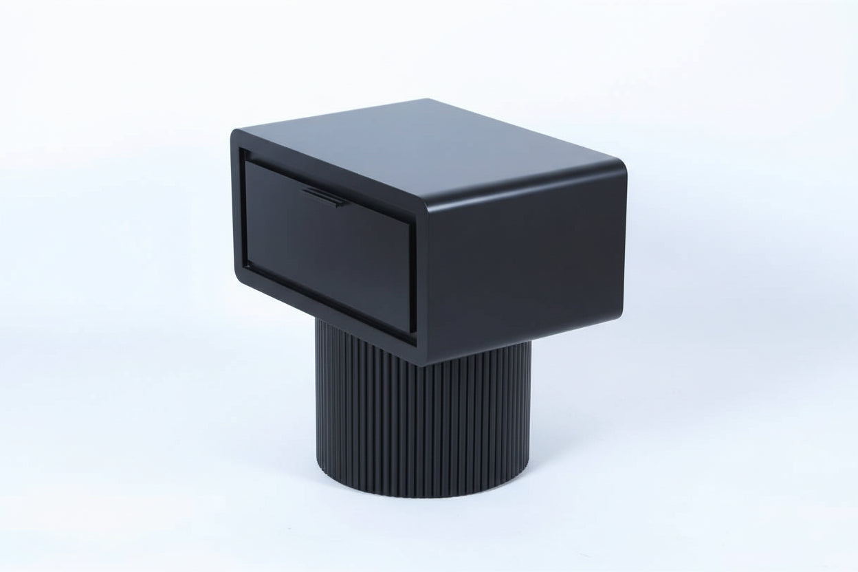 Black side table with cylindrical base on a light wood floor.