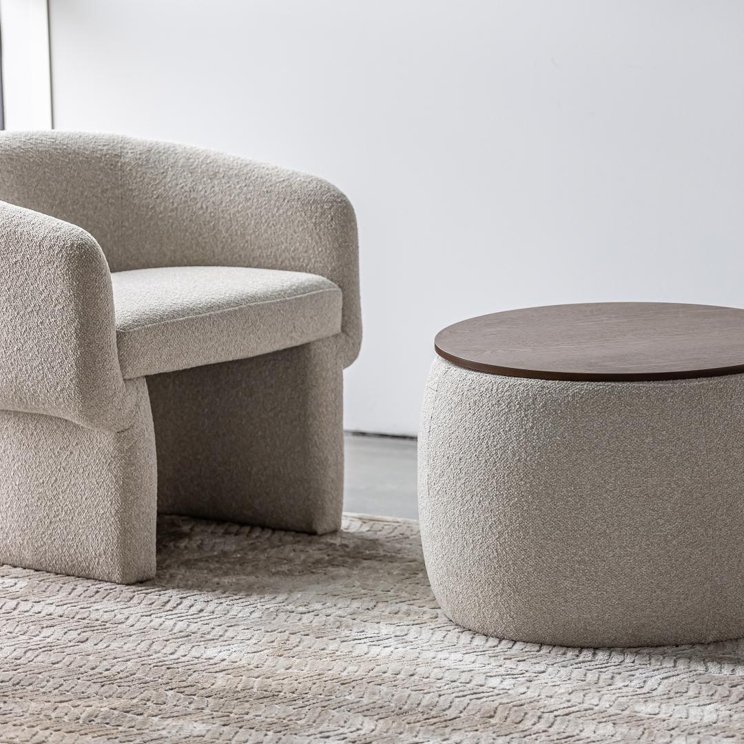 Beige textured armchair and round ottoman in a minimalistic room.