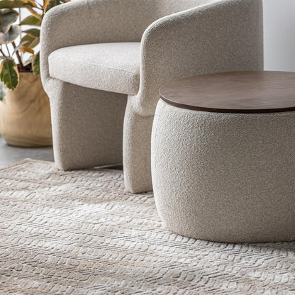 Beige textured armchair and round table in a room with a textured rug and plant.