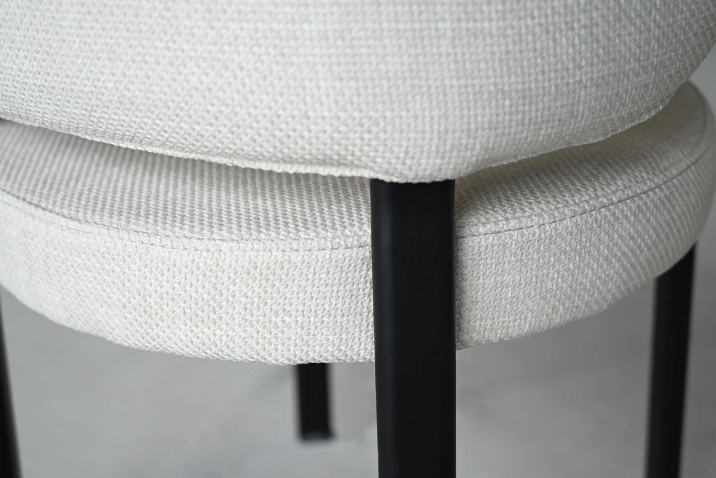 Close-up of a chair with white cushioned seat and black metal legs on a neutral background
