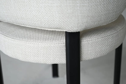 Close-up of a chair with white cushioned seat and black metal legs on a neutral background