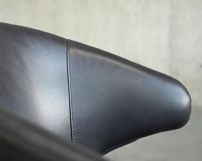 Close-up of a black leather dining chair with a blurred background