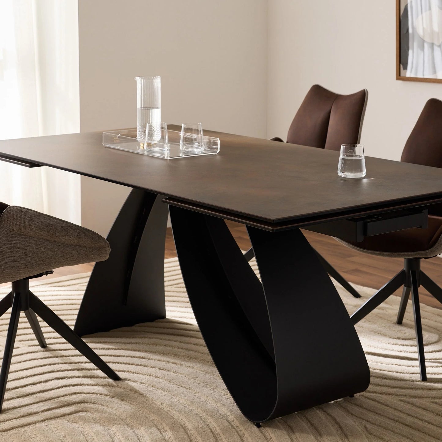 Modern dining table with black legs and brown chairs in a room with light-colored walls and wooden floor.