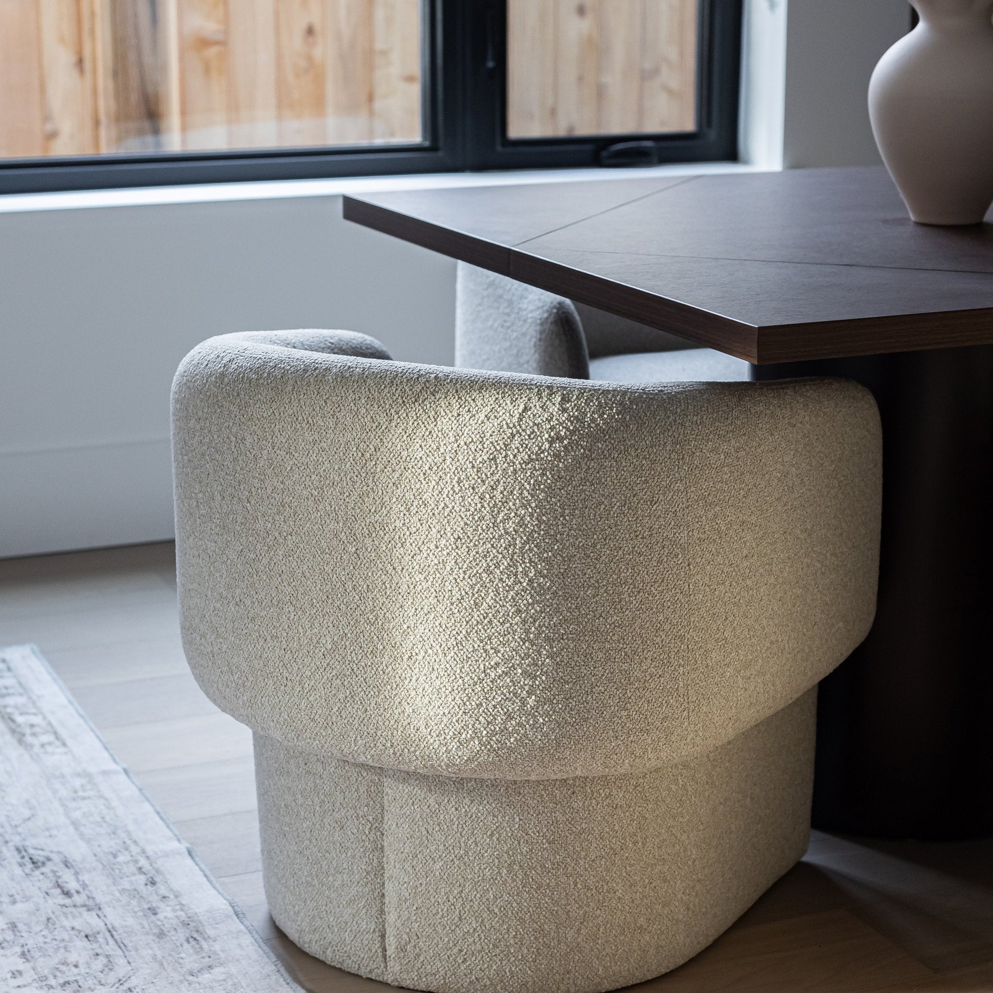 Beige textured chair next to a wooden table in a room with a window.