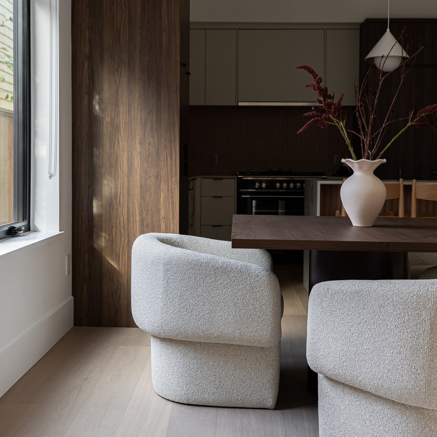 Modern living room with gray chairs, a wooden table, and kitchen in the background.