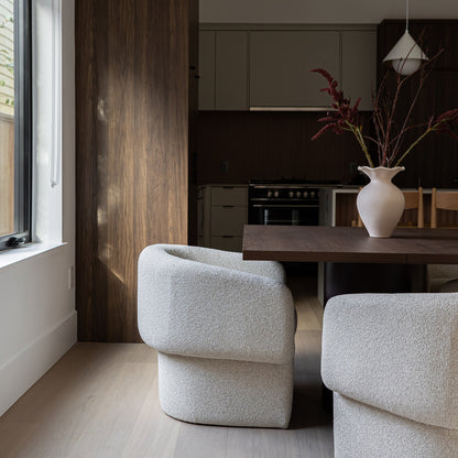 Modern living room with gray chairs, a wooden table, and kitchen in the background.