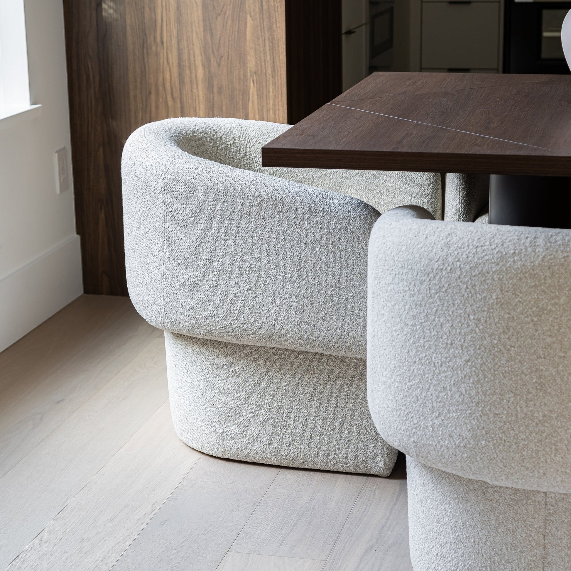 Two textured white chairs in a room with a wooden floor and table.