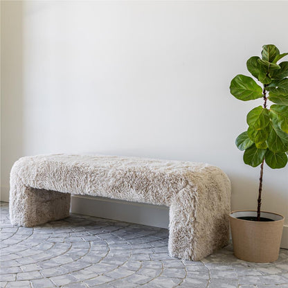 Fluffy white bench next to a potted plant on a stone floor with a white wall background