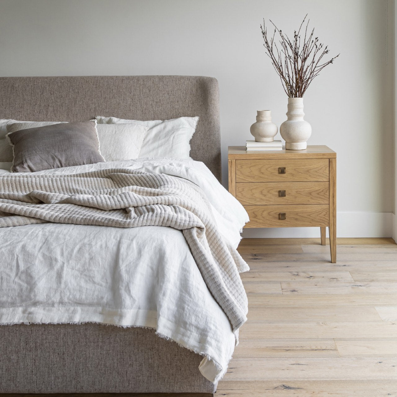 Neatly made bed with gray bedding and white pillows, wooden nightstand with decorative items.