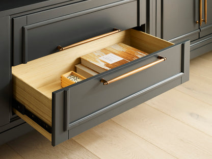 Open drawer with wooden items inside, featuring a gold handle on a light wood floor.