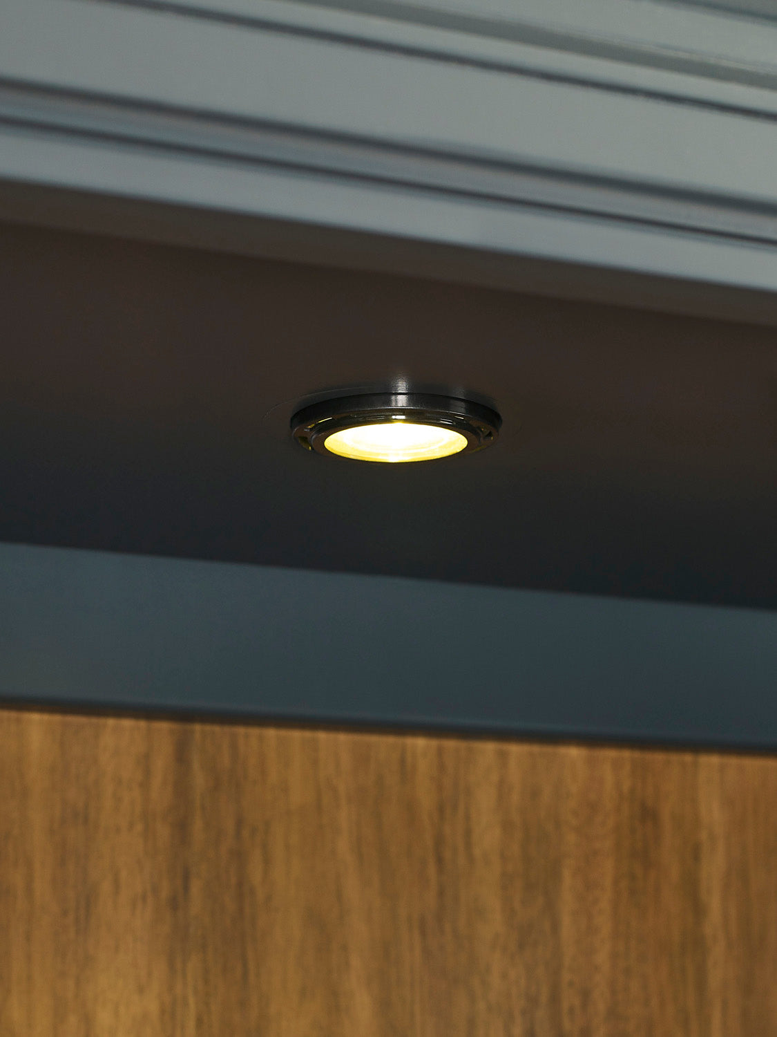 Small round ceiling light fixture on a dark ceiling with wooden paneling.