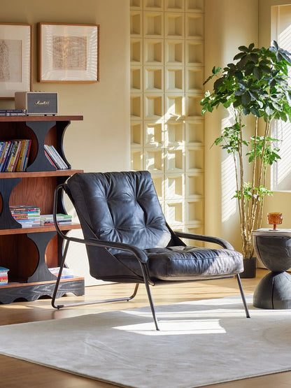 Modern black armchair in a living room with a bookshelf and decorative elements.
