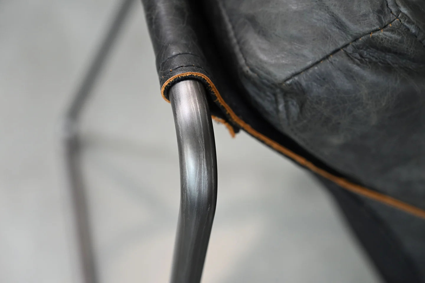 Close-up of a black leather chair with a metal armrest on a neutral background
