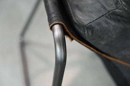 Close-up of a black leather chair with a metal armrest on a neutral background