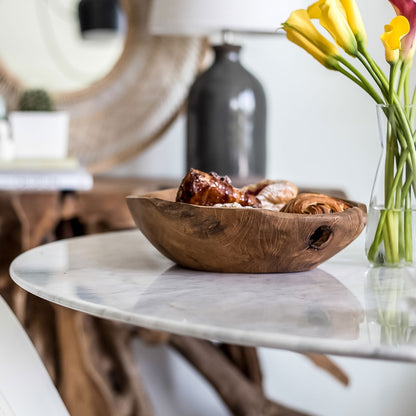 Wooden bowl with food on a marble table, with a vase of flowers in the background.