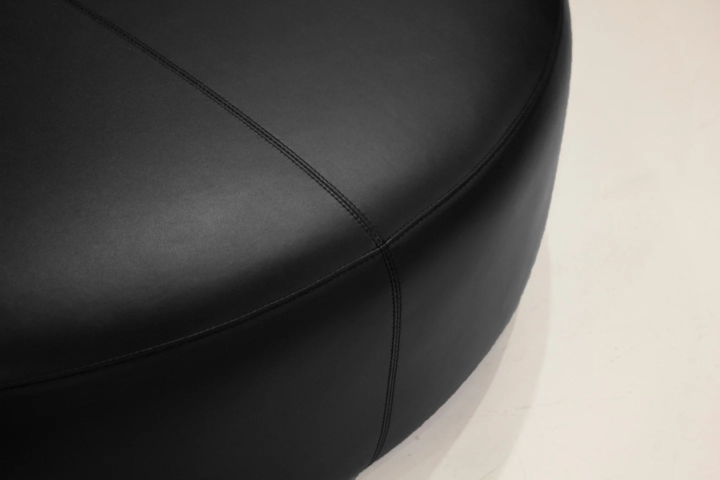Close-up of a black leather seat with visible stitching on a beige background