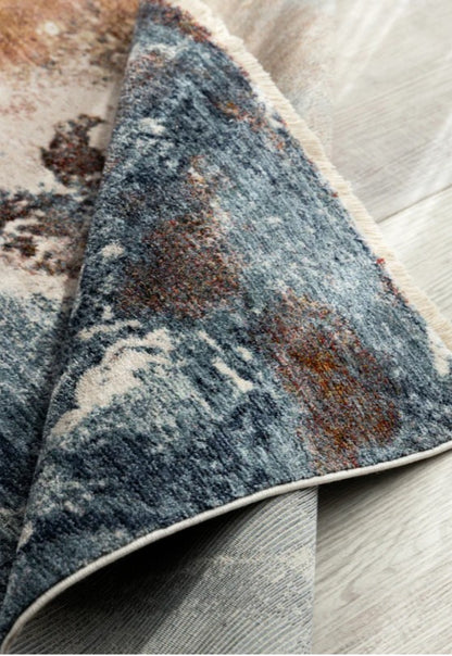 Close-up of a textured blue and brown area rug on a light wood floor.