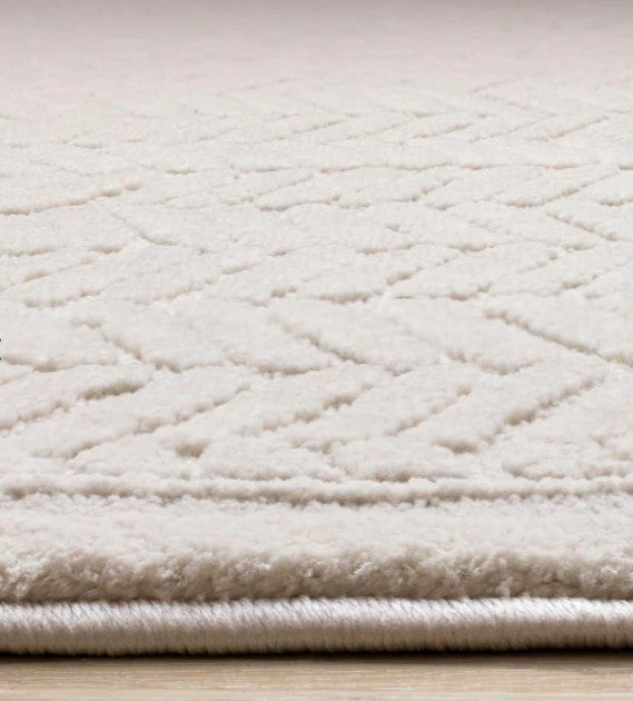 Close-up of a textured beige rug with a diamond pattern on a light wooden floor.