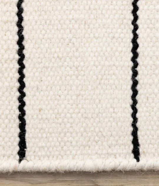 Close-up of a white rug with black stripes on a wooden floor.