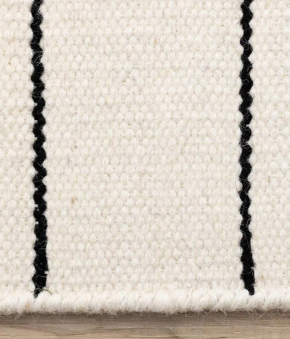 Close-up of a white rug with black stripes on a wooden floor.