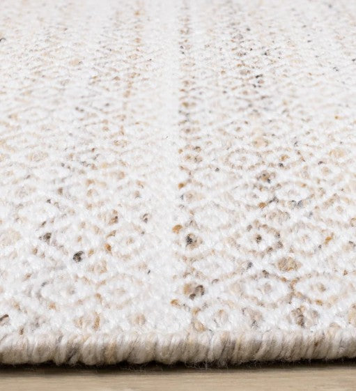 Close-up of a textured beige and white rug on a wooden floor.