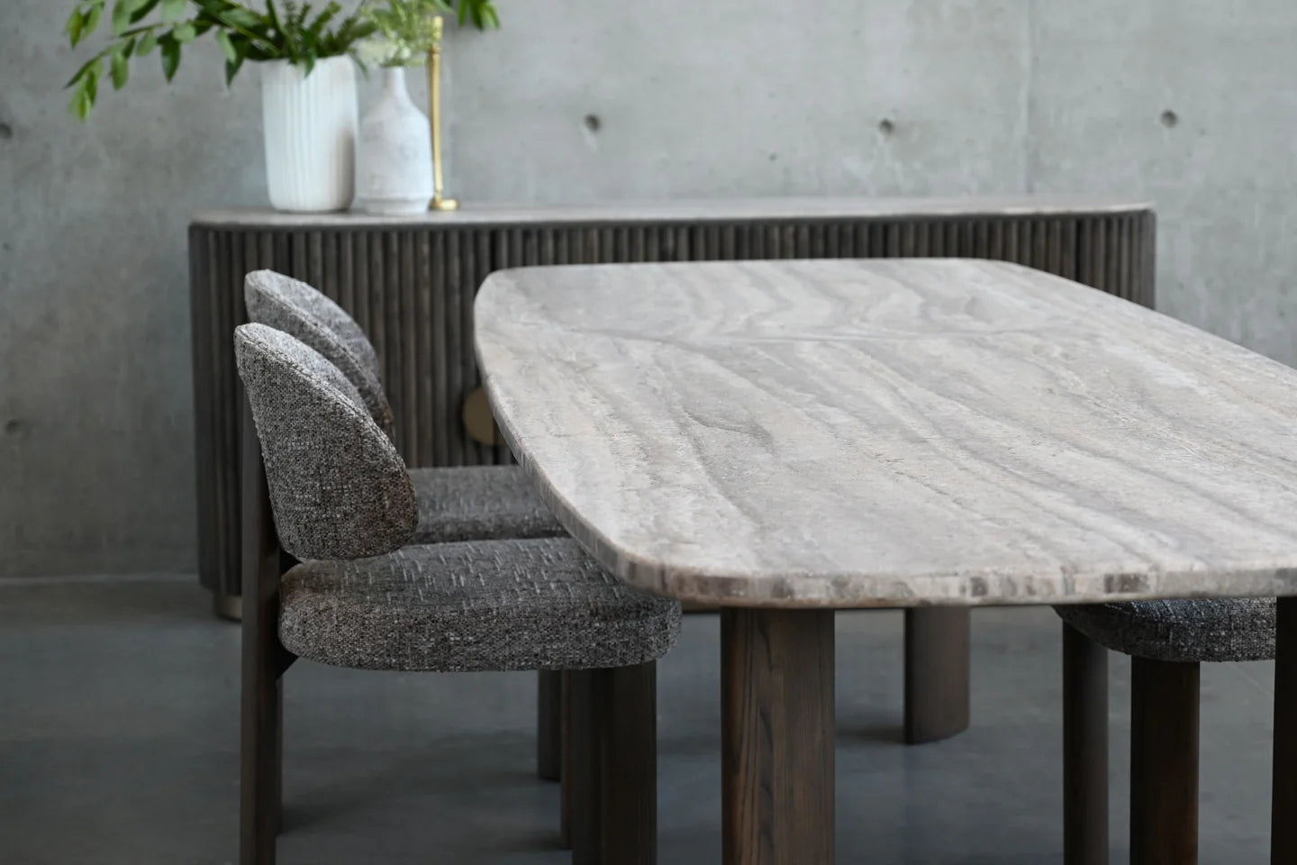 Dining table with marble-like surface and four chairs in a room with concrete walls.