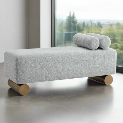 Gray upholstered bench with wooden legs and cylindrical cushions in a modern interior setting.