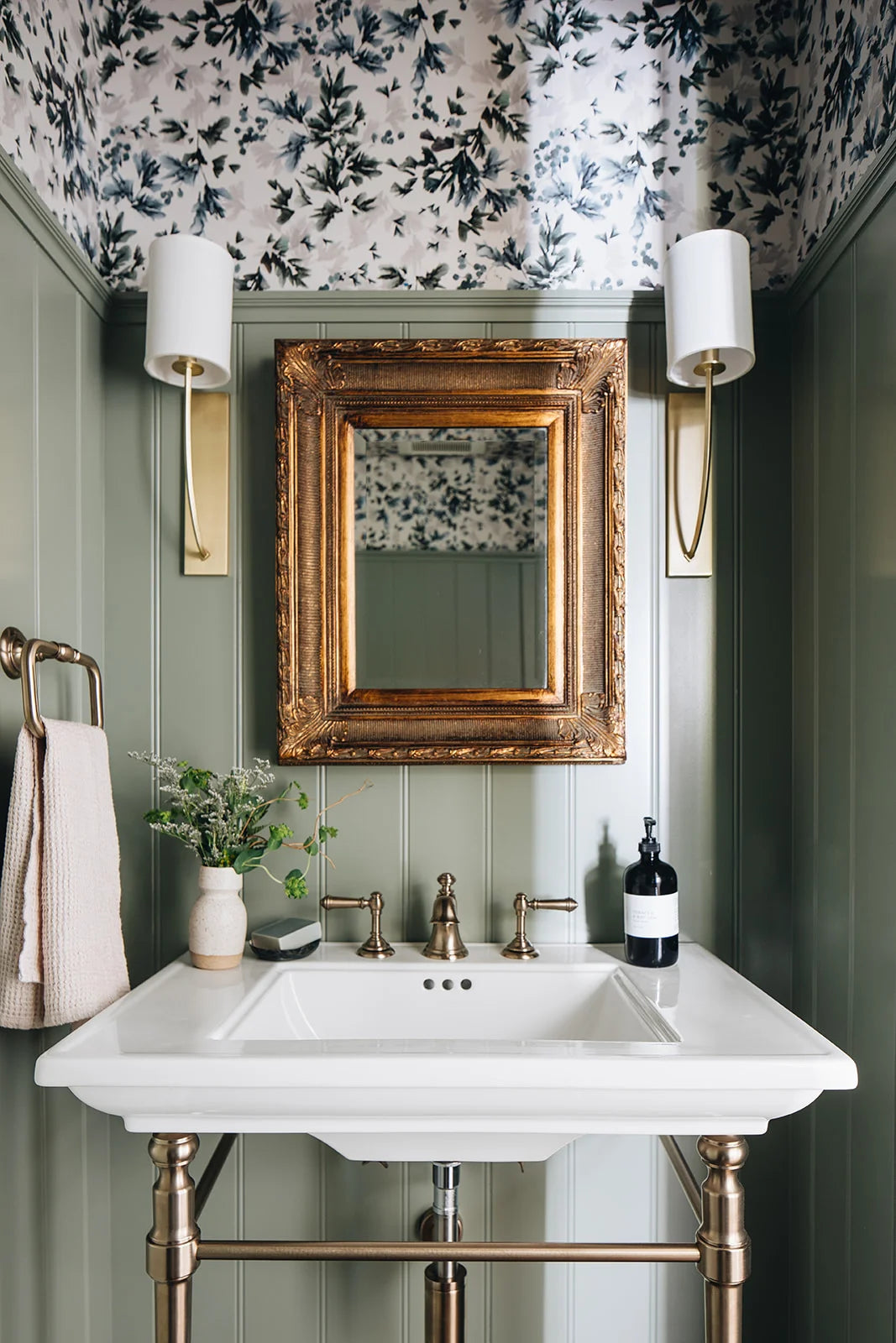 Bathroom with floral wallpaper, gold-framed mirror, and white sink.