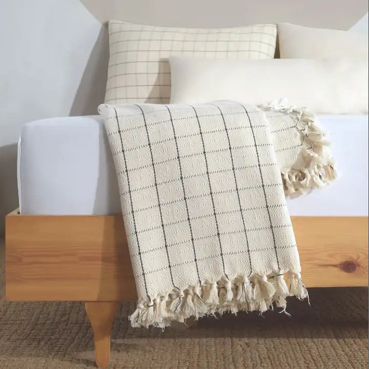 Beige checkered blanket with tassels draped over a wooden bed frame.