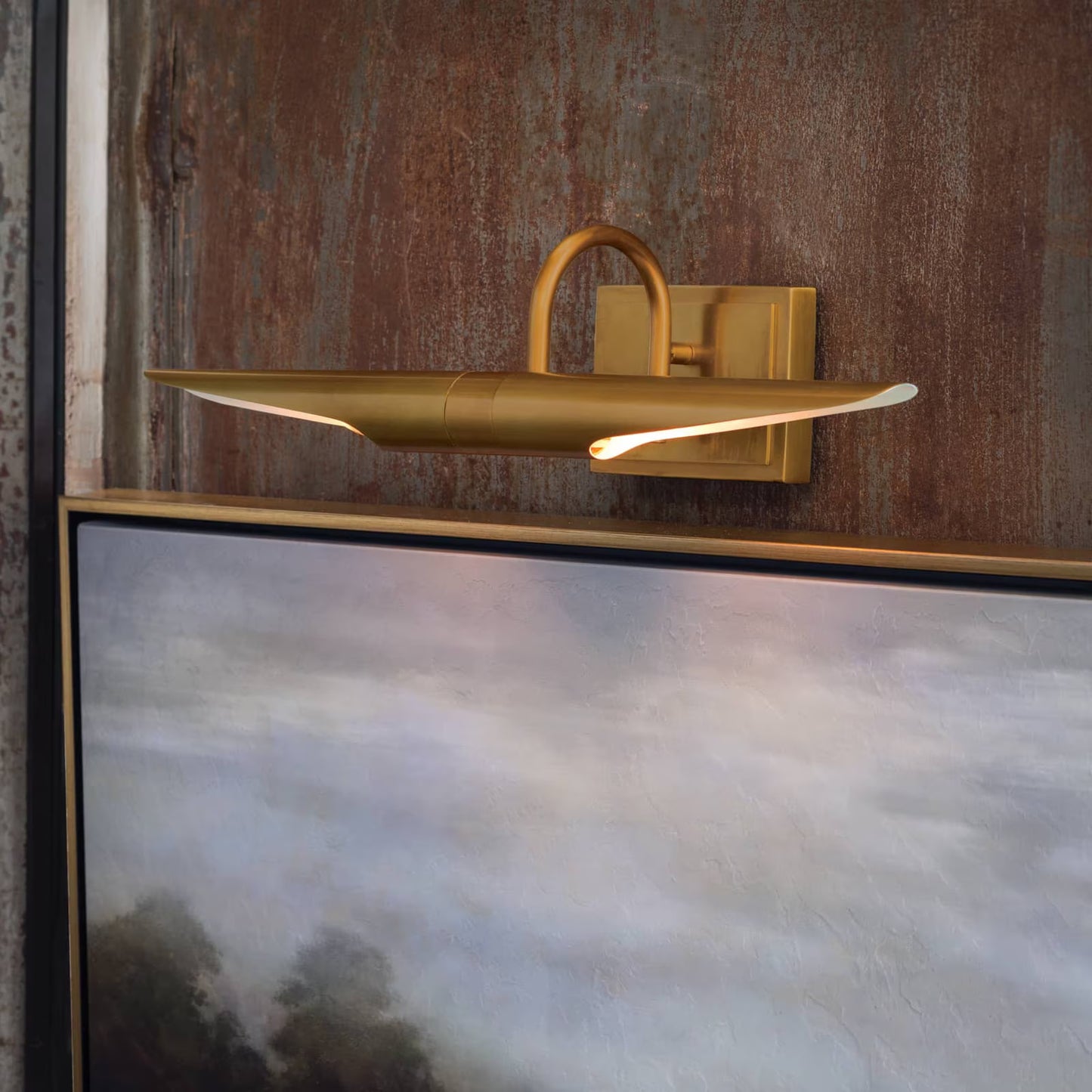 Gold wall-mounted light fixture on a textured wall with a painting below