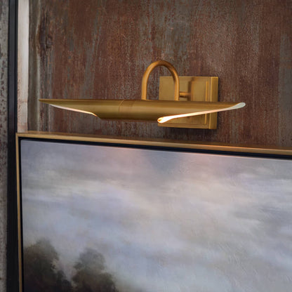 Gold wall-mounted light fixture on a textured wall with a painting below
