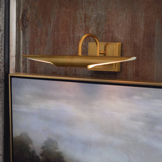 Gold wall-mounted light fixture on a textured wall with a painting below