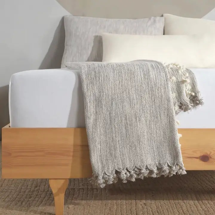 Gray textured blanket draped over a wooden bench with pillows in the background