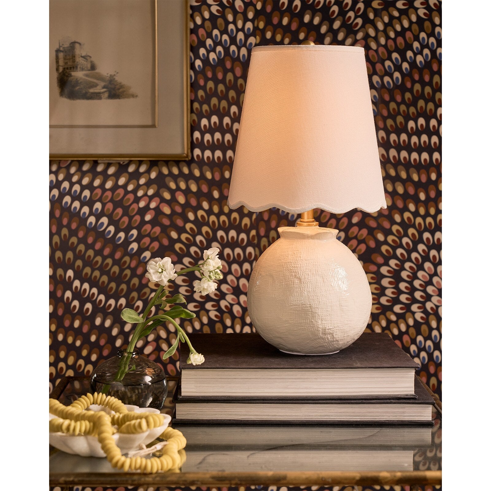 White ceramic lamp on a stack of books against a patterned wall.