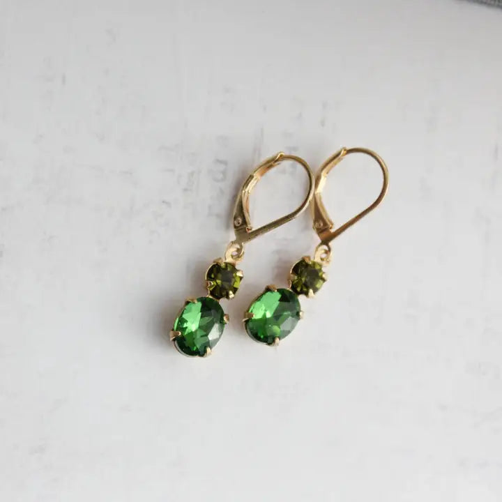 Gold earrings with green gemstones on a light gray background